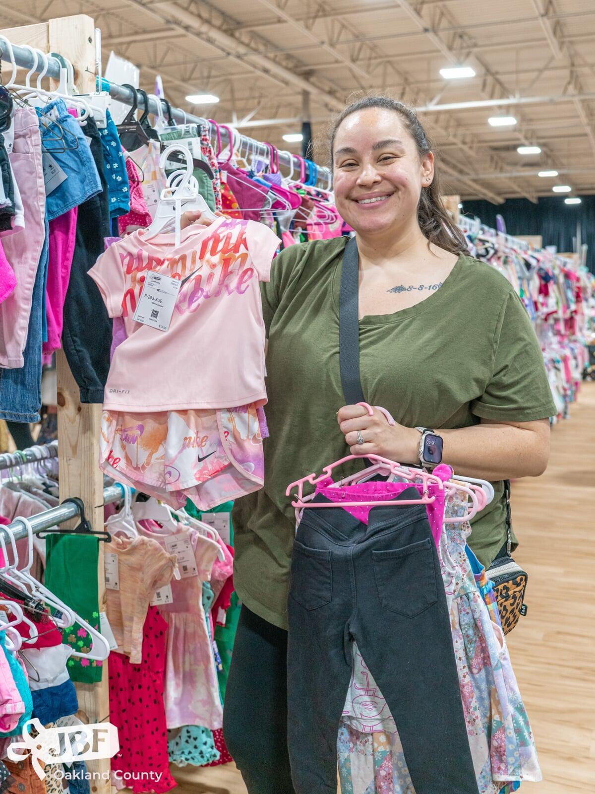 Beautiful mom holds two boys tops—one in each hand—as she shops the deals at her local sale.