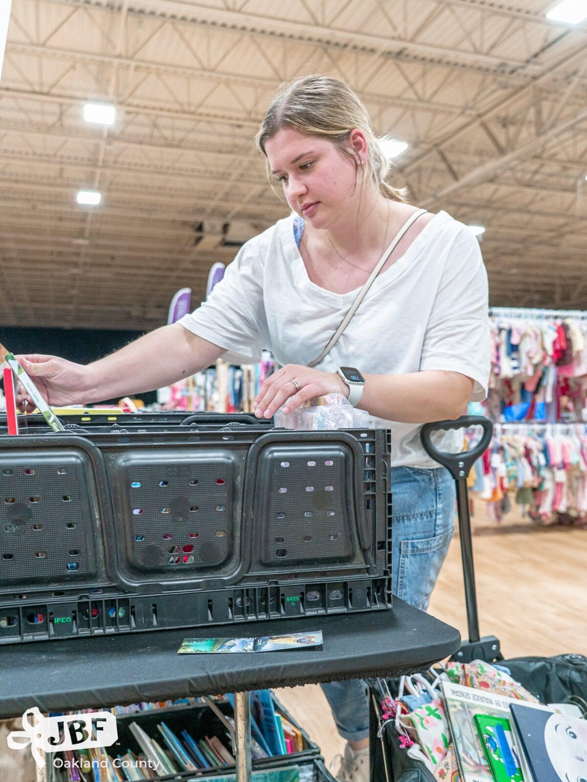 Two masked moms—one holding a child with a mask, the other pregnant—shop for their families at the local JBF sale.